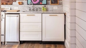 Cocina con alacenas blancas, pared de ladrillo e impresión de arte pop.