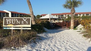 Un cartel de 'Siesta Dunes' con un camino bordeando la playa que lleva a un edificio de techo rojo.
