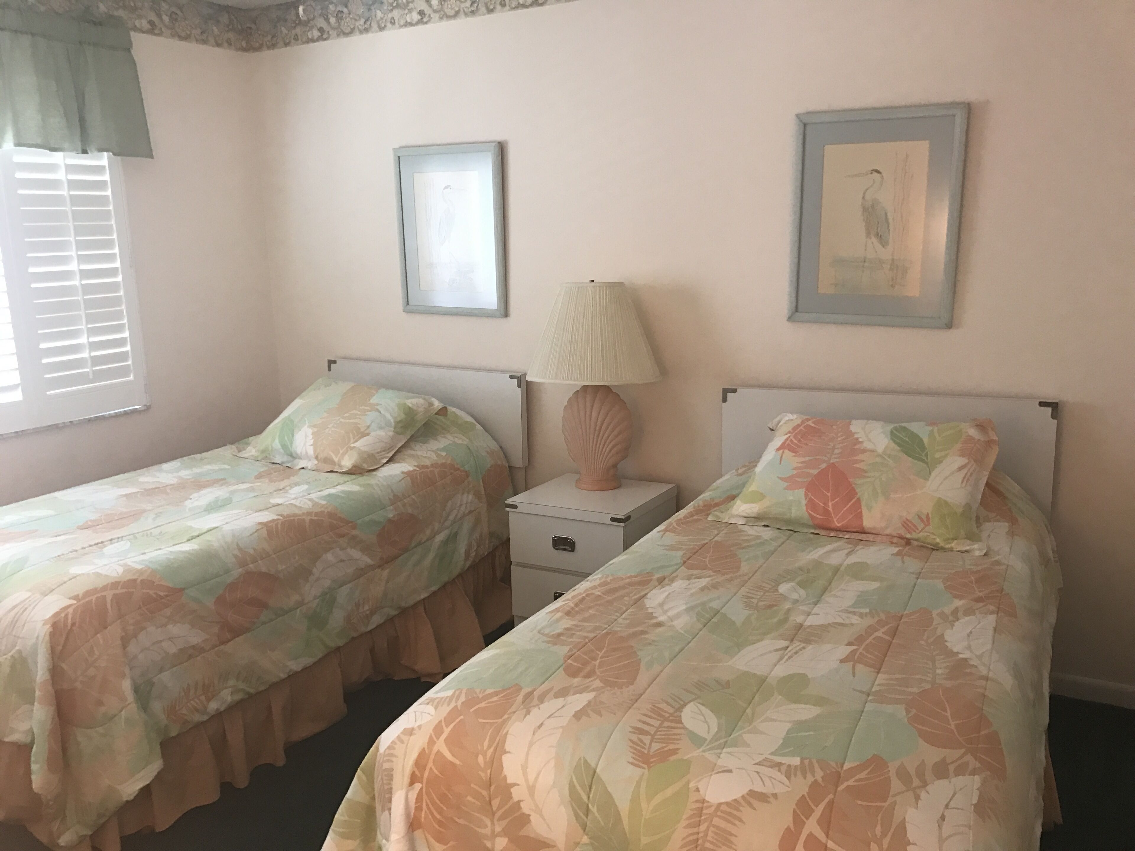 A bedroom with two single beds, a nightstand with a lamp, and two framed pictures on the wall.