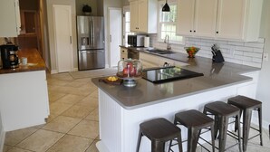 A modern kitchen with white cabinetry, a large island with bar stools, stainless steel appliances, and a hanging pendant light. - Willow Pond Nashville, A Private Luxury Five-Star Farmhouse Great for Lg Groups! (Pleasant View)