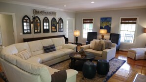 A living room with a beige sectional sofa, a smaller sofa, two armchairs, a coffee table, and a rug. There are three arched windows with blinds, a painting on the wall, and a sign above the windows. - Willow Pond Nashville, A Private Luxury Five-Star Farmhouse Great for Lg Groups! (Pleasant View)