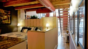 Habitación de hotel con cama, lámparas de noche, techo de madera y vistas al exterior.