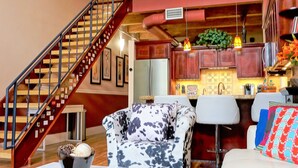 Una sala de estar con un sofá, una mesa de centro y un sillón estampado. Se observa una escalera con barandilla que conduce a un nivel superior.