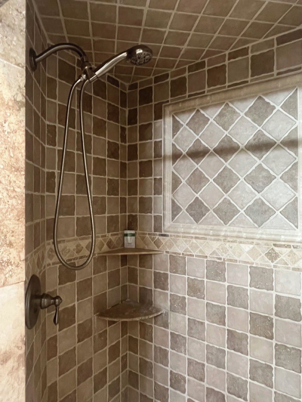 A shower area with a tiled wall, a showerhead, and a small shelf with a bottle.