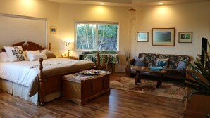 A bedroom with a bed, bedside table, and a window with a view of trees. - SUPER SPACIOUS! Privacy entrance. Comfortable and cozy. Quiet and peaceful! (Waikoloa Village)