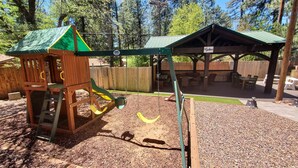 A playground with a wooden play structure, swings, and a covered seating area. - Christopher Creek Cabins - Cabin 6 (Payson)