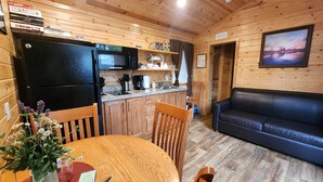 A cozy cabin-style room with a wooden interior, a dining table with chairs, a black refrigerator, a microwave, a coffee maker, and a black leather couch. - Christopher Creek Cabins - Cabin 6 (Payson)