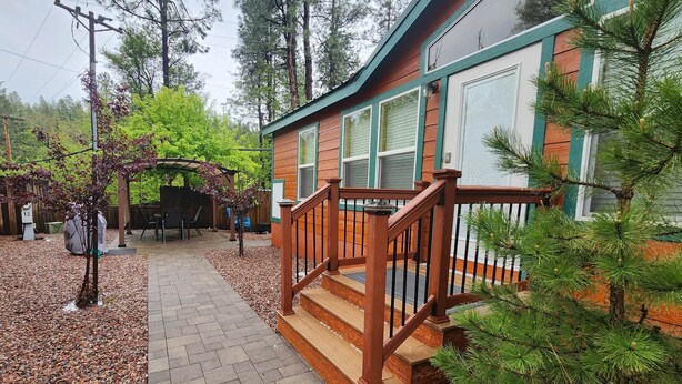 A wooden staircase leading to a porch with a covered seating area and a small tree in the foreground. - Christopher Creek Cabins - Cabin 6 (Payson)