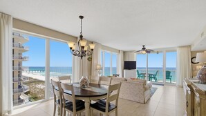 A spacious living area with a dining table, chairs, a sofa, and a TV. Large windows offer a view of the beach and ocean. - Summer Salt -Beautiful Condo- spectacular views (Navarre)