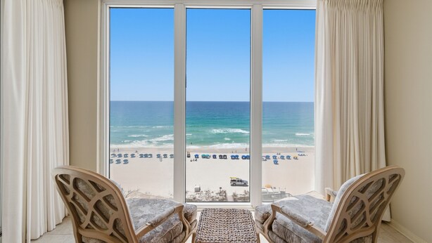 A room with a large window overlooking a beach, two chairs, and a small table. - Summer Salt -Beautiful Condo- spectacular views (Navarre)