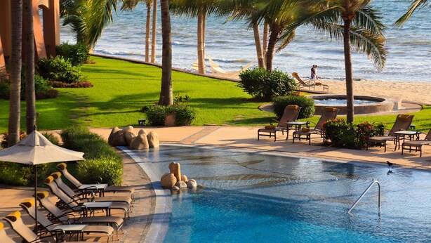 A pool area with lounge chairs, a small pool, and a view of the ocean.