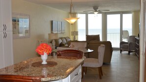 A kitchen with a granite countertop, a vase with flowers, and a dining area with a table and chairs. - Direct Oceanfront, Newly Renovated 2-Bedroom, 2-Bath Condo - No Drive Beach (Daytona Beach Shores)