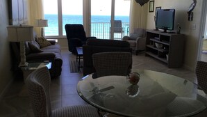 A living room with a glass table, sofas, chairs, a TV, and a balcony with a view of the sea. - Direct Oceanfront, Newly Renovated 2-Bedroom, 2-Bath Condo - No Drive Beach (Daytona Beach Shores)