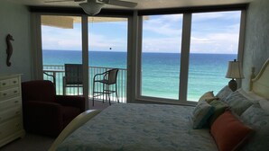 A bedroom with a large bed, a chair, a dresser, and a balcony with a view of the ocean. - Direct Oceanfront, Newly Renovated 2-Bedroom, 2-Bath Condo - No Drive Beach (Daytona Beach Shores)