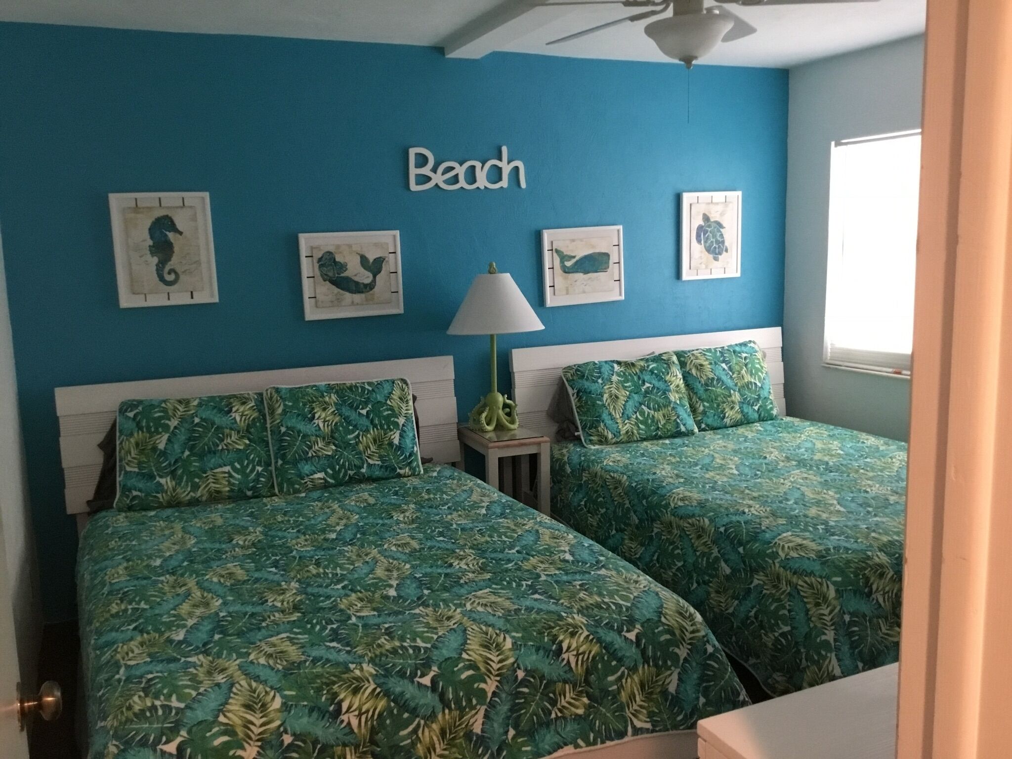 A bedroom with two beds, a ceiling fan, and wall art depicting sea creatures.