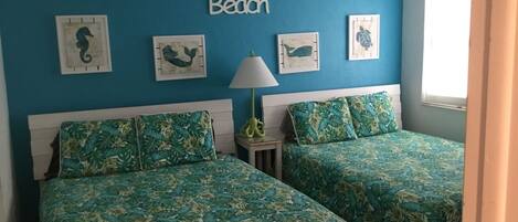 A bedroom with two beds, a ceiling fan, and wall art depicting sea creatures.