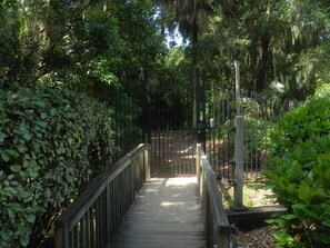 Walk along the winding boardwalk surrounded by lush greenery and trees, leading to a secure gated entrance.