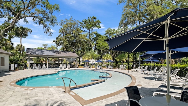 A swimming pool with lounge chairs and umbrellas, surrounded by trees and a covered seating area. - Brigantine Quarters, Shipyard. Unit 292. 2BD/1.5Ba (Hilton Head Island)