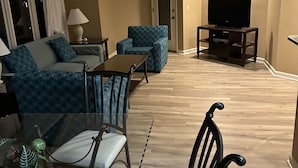 A modern living room with a sofa, a dining table with chairs, a TV on a stand, and a ceiling fan. - Brigantine Quarters, Shipyard. Unit 292. 2BD/1.5Ba (Hilton Head Island)