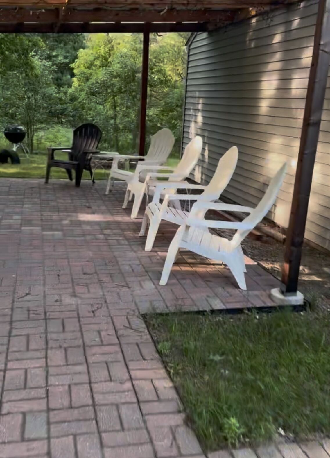 A covered patio with brick flooring and white Adirondack chairs.