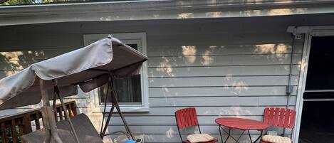 Eine Holzterrasse mit einem chevron-gestreiften Teppich, einer Schaukel und Gartenmöbeln, darunter ein Tisch und Stühle.