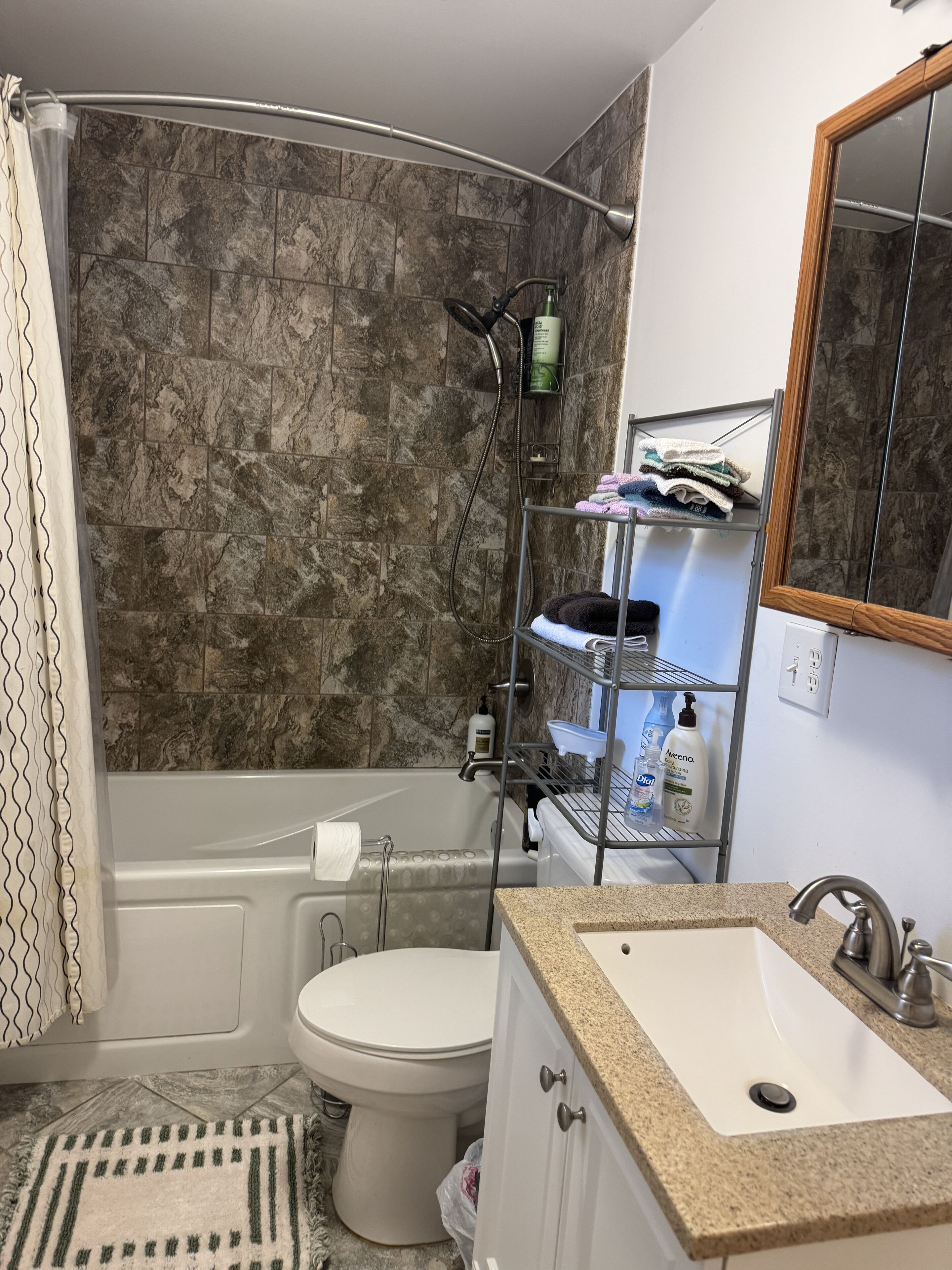 Un baño con ducha, inodoro, lavamanos y un perchero para toallas.