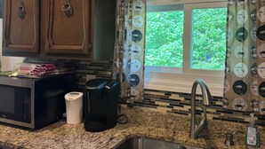 Una cocina con armarios de madera, microondas, cafetera y ventana con vistas a vegetación.
