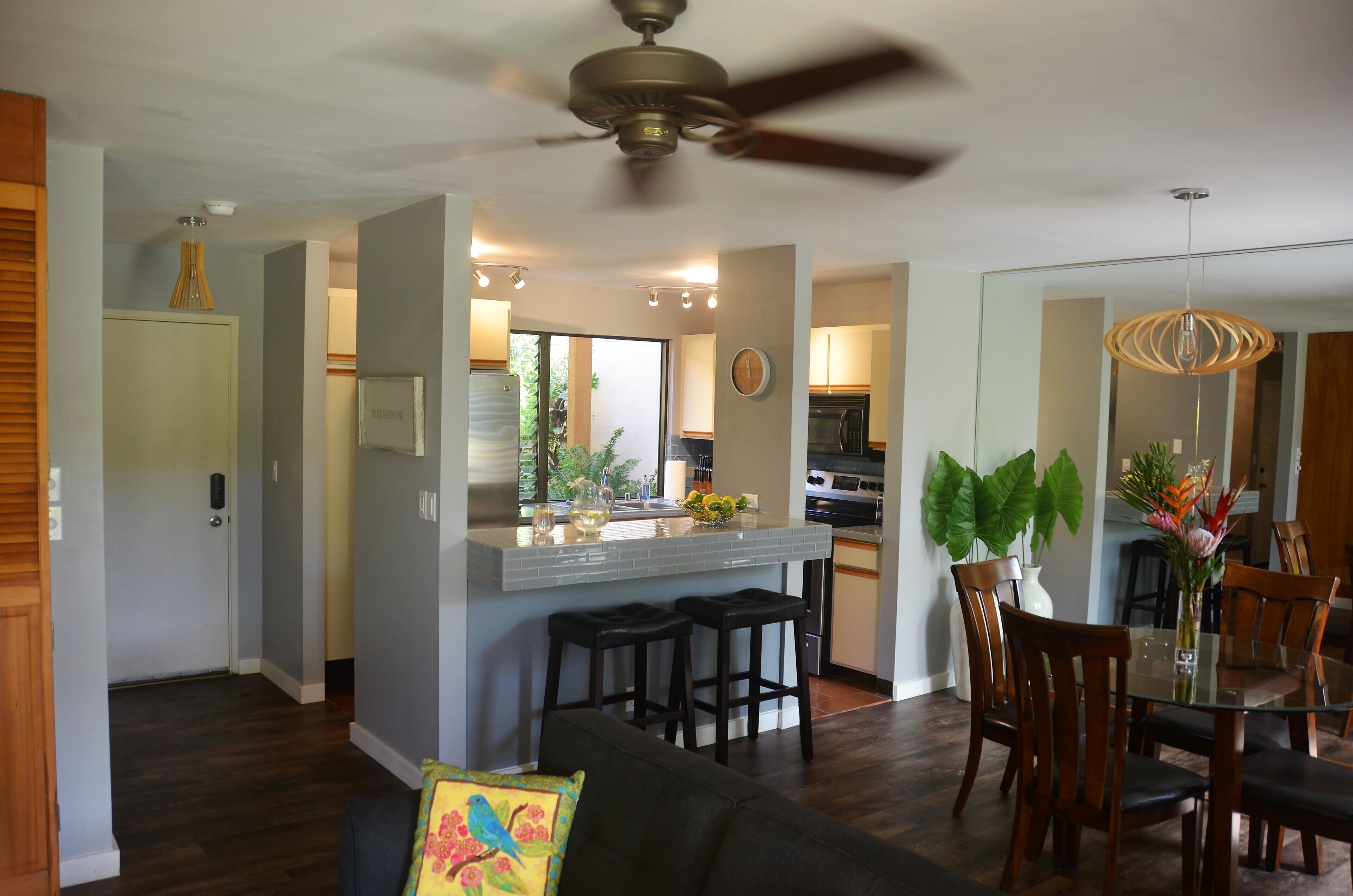 A modern kitchen with a central island, bar stools, and a dining area with a glass table and wooden chairs.