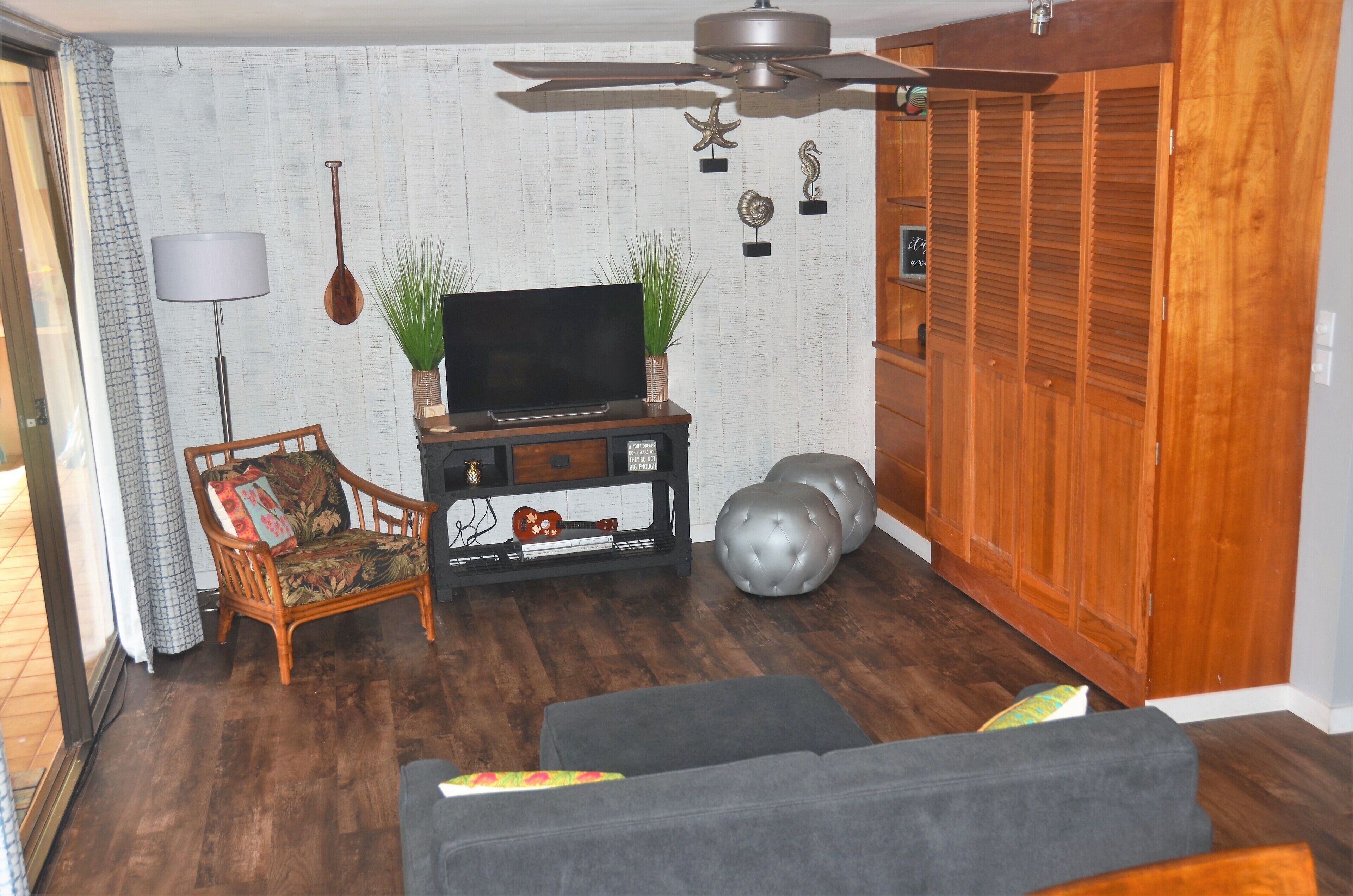 Una sala de estar con televisor, un mueble de madera, un sofá y un ventilador de techo.