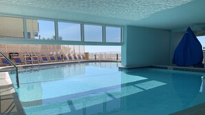 Una piscina interior con agua cristalina, suelo de baldosas y vistas al cielo a través de amplios ventanales.