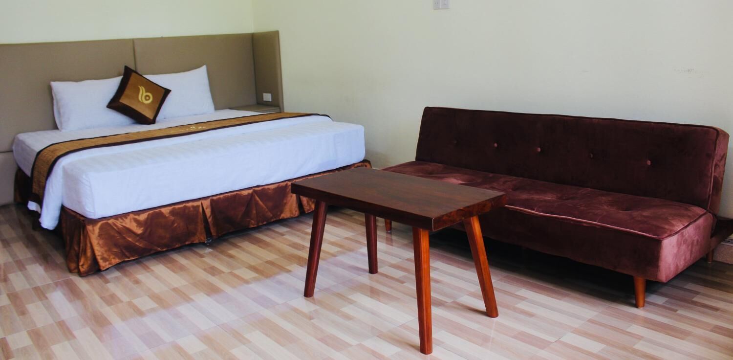 A hotel room with a bed, a wooden table, and a red sofa.