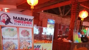 A wooden dining table with chairs, a menu board for Mabuhay Thresher Dive Resort, and a traditional lantern. - Mabuhay Thresher Dive (Daanbantayan)