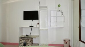A room with a flat-screen TV mounted on the wall, a small desk with a chair, a trash bin, and a green desk lamp. - Mabuhay Thresher Dive (Daanbantayan)