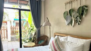 Quarto com cama, cadeira de vime, planta pendente e vista para o exterior.