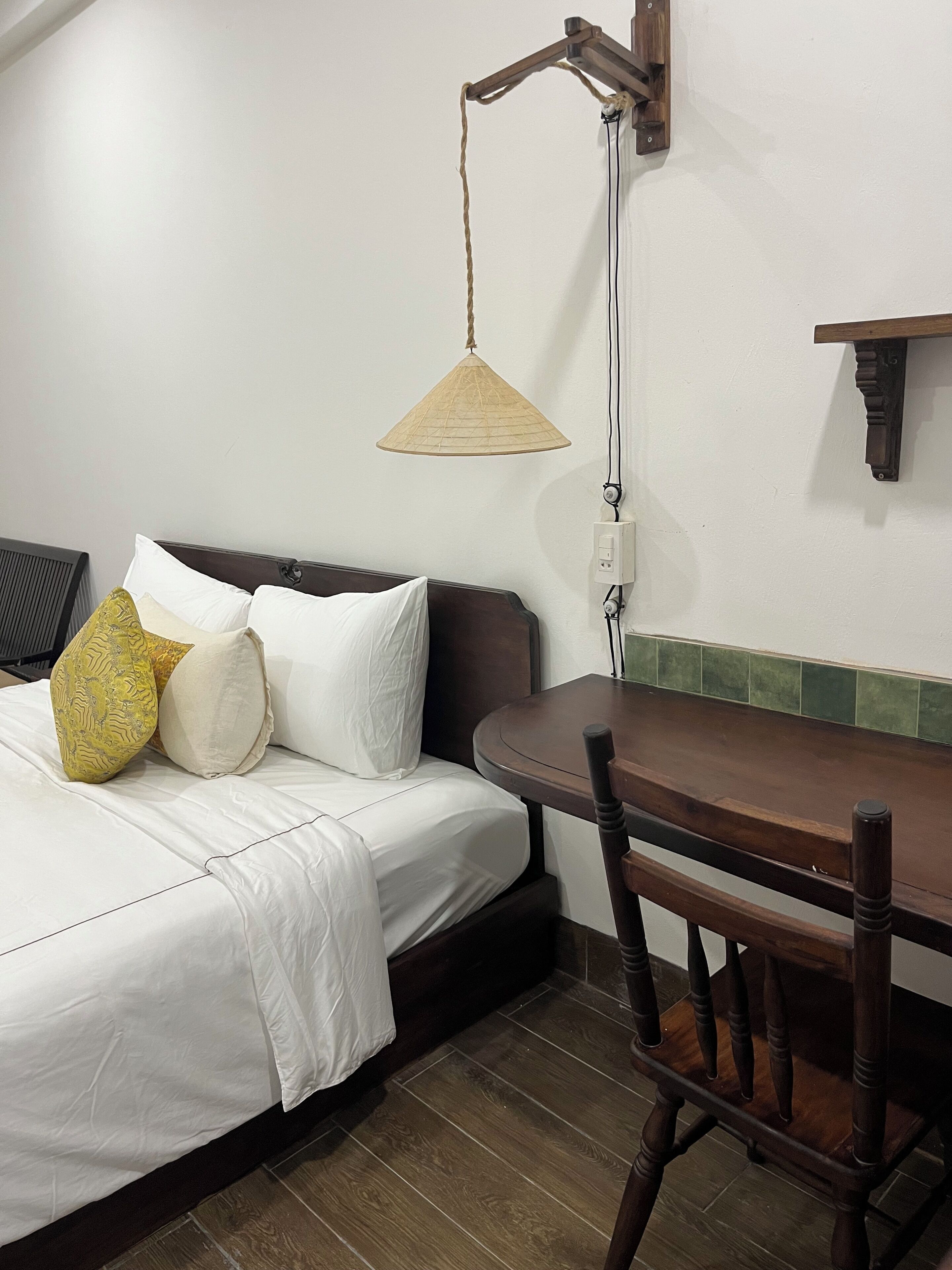 A bed with white bedding, a wooden table, and a hanging lamp.