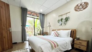 Quarto com cama, mesas de cabeceira, cesta de vime e planta pendente, com vista para o exterior.