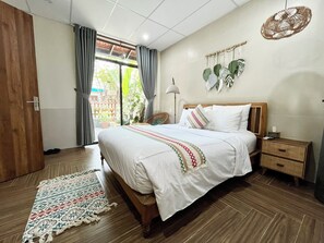 A bedroom with a bed, bedside tables, a nightstand, a woven basket, a hanging plant, and a view of the outdoors. - Hue Sweethouse 2 Homestay (Hue)