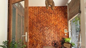 Uma porta de madeira, parede com padrão herringbone, um banco de madeira, um ventilador e um vaso com planta.