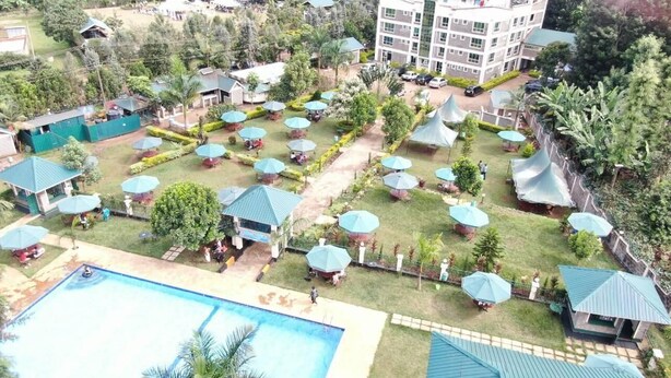 Vista aérea de un complejo turístico con varias zonas de estar al aire libre, una piscina y un edificio grande al fondo.