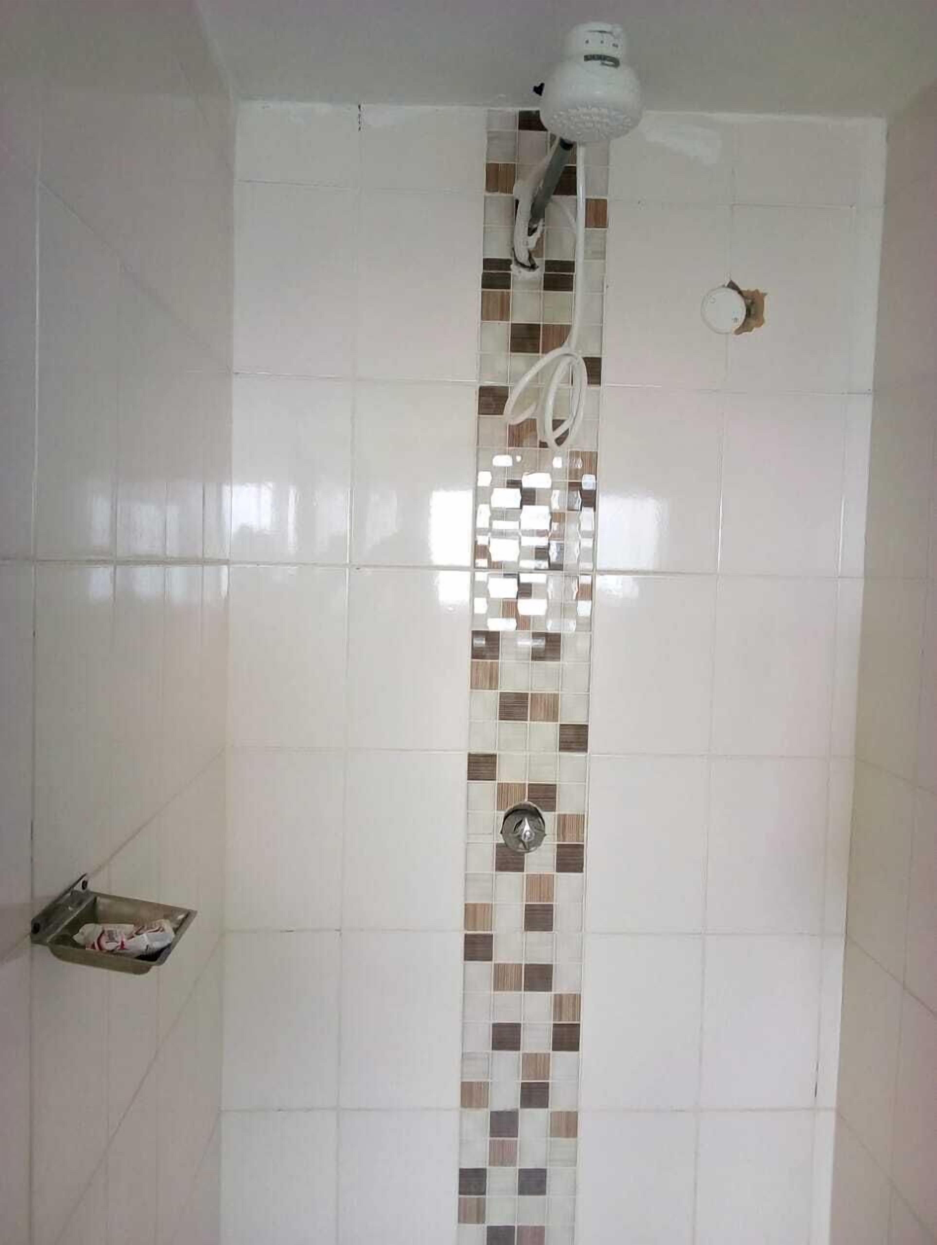 A bathroom with white tiles, a shower with a mosaic tile design, and a small shelf with a magazine.