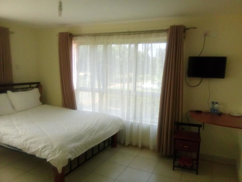 A hotel room with a bed, a TV mounted on the wall, a desk with a chair, and a window with curtains.