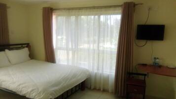 A hotel room with a bed, a TV mounted on the wall, a desk with a chair, and a window with curtains.