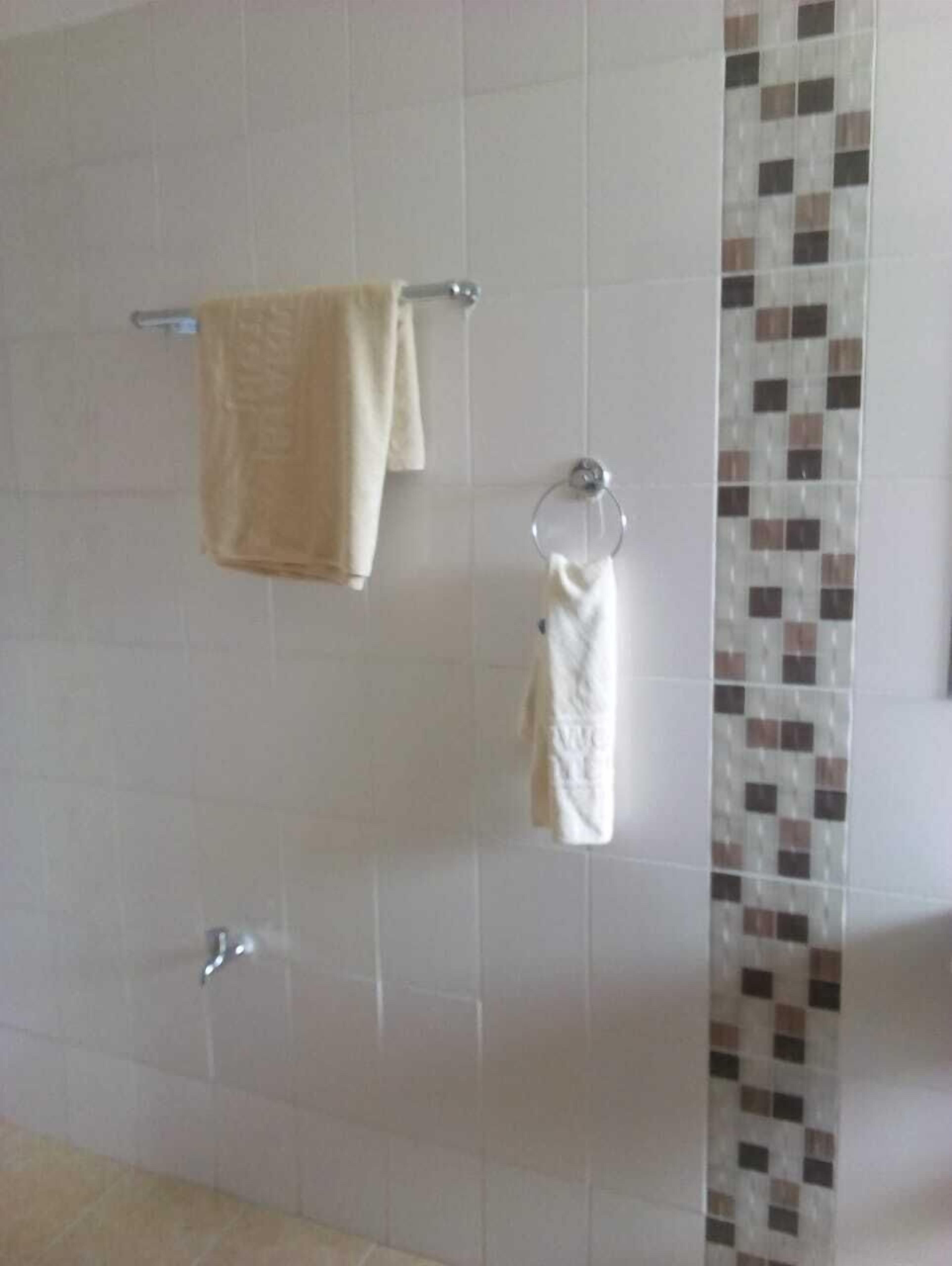 Um banheiro com paredes revestidas de azulejos brancos, uma toalha bege em um porta-toalhas, uma toalha branca em um suporte circular e uma parede de destaque com azulejos estampados.