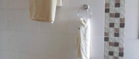 Um banheiro com paredes revestidas de azulejos brancos, uma toalha bege em um porta-toalhas, uma toalha branca em um suporte circular e uma parede de destaque com azulejos estampados.