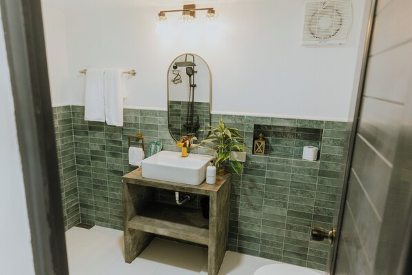 A bathroom with a wooden vanity, a white sink, a mirror, a towel rack, a shower, and green tiled walls. - Bintana Sa Paraiso Binunsaran (Mambajao)
