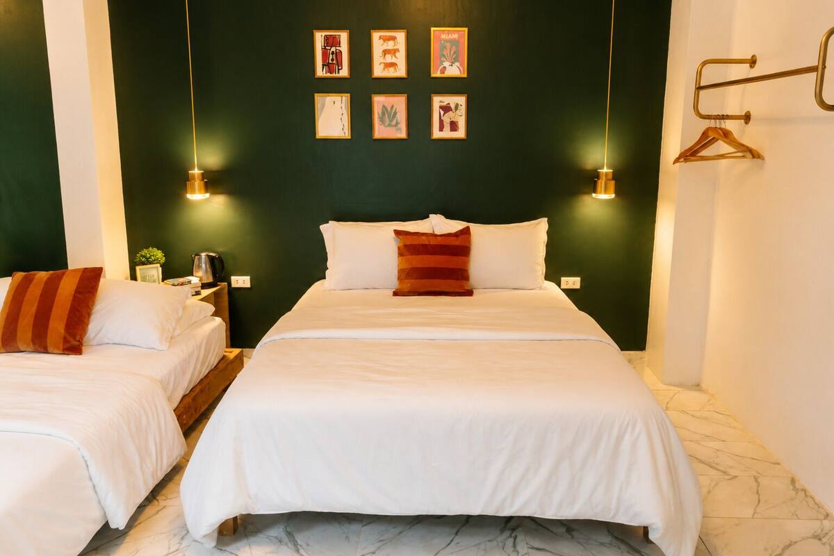 Habitación de hotel con dos camas, una pared de acento color verde oscuro y obras de arte enmarcadas.
