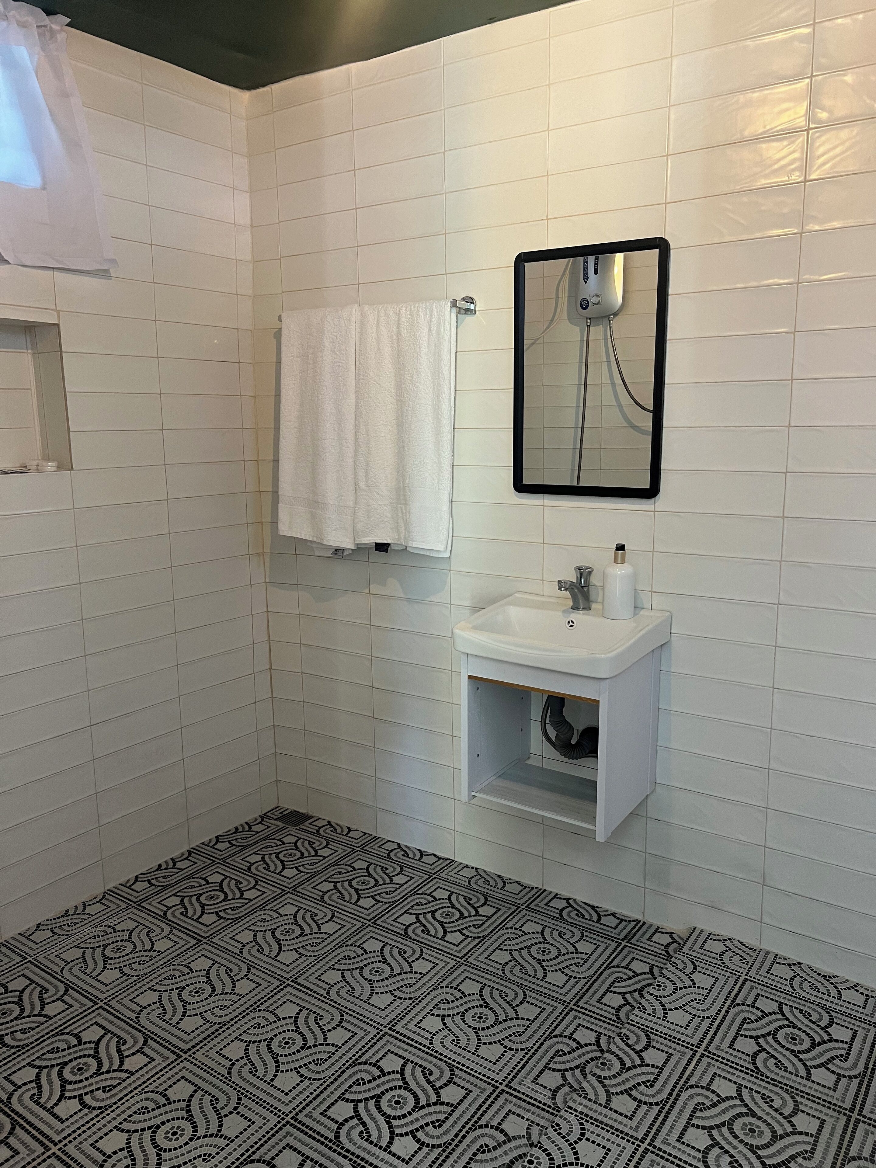 Un baño con paredes de azulejos blancos, un lavabo blanco, un espejo y una ducha.