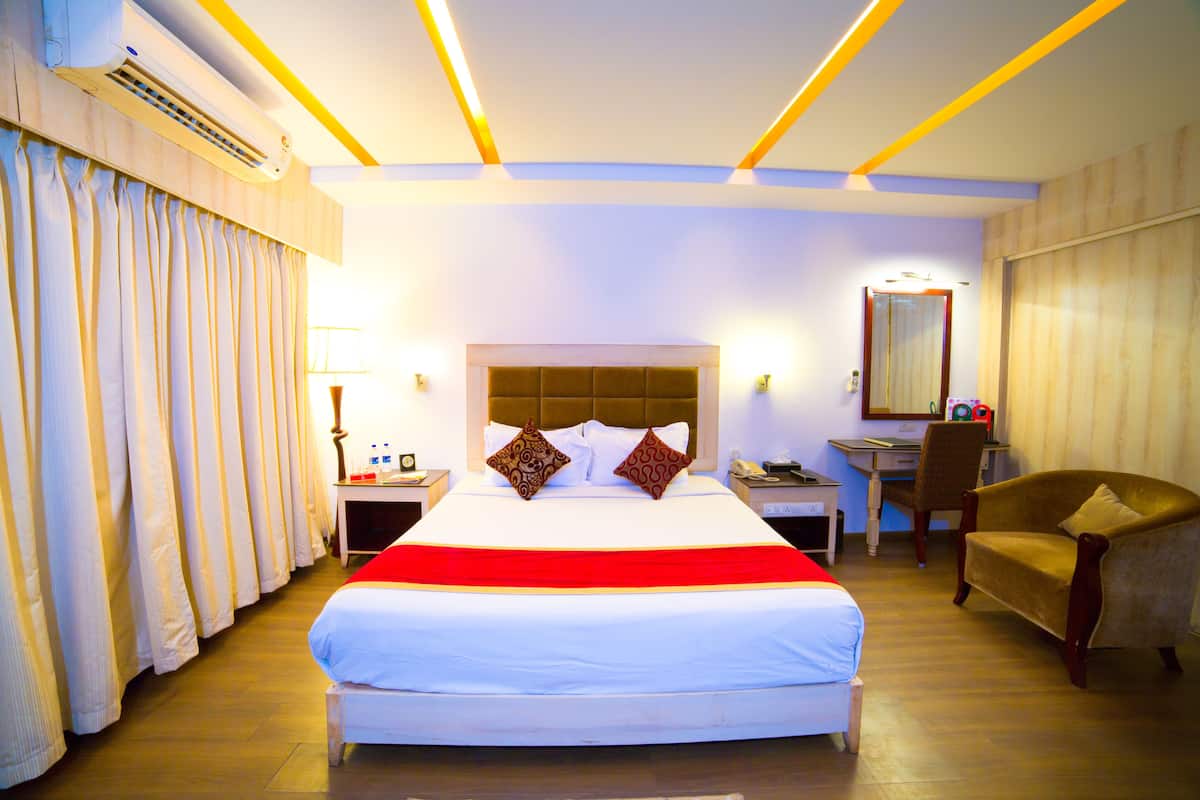 A hotel room with a large bed, a desk, a chair, and an air conditioning unit.