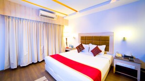 A hotel room with a large bed, a nightstand with a lamp, a phone, and an air conditioning unit.