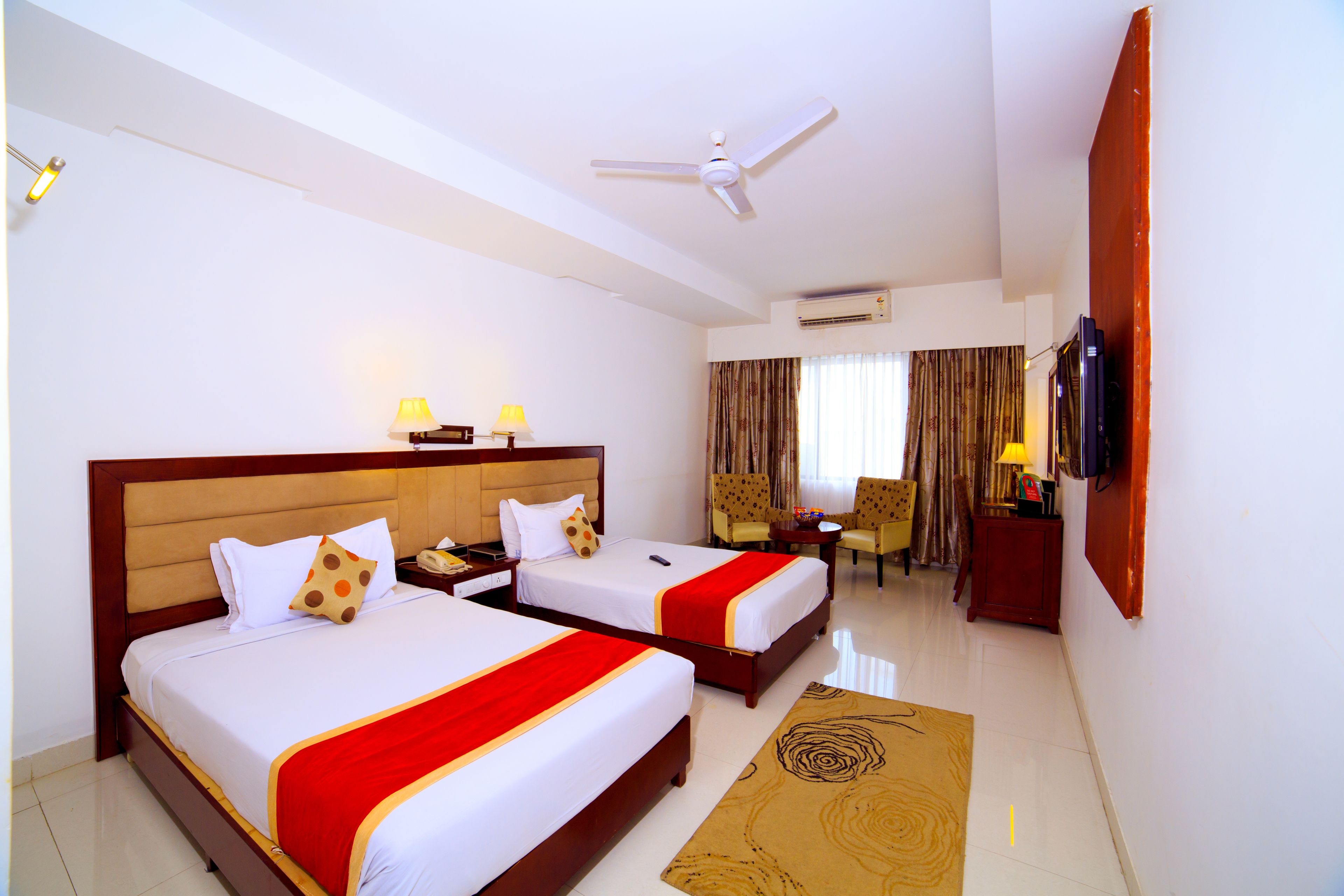 A hotel room with two beds, a desk, a chair, a television, and a ceiling fan.